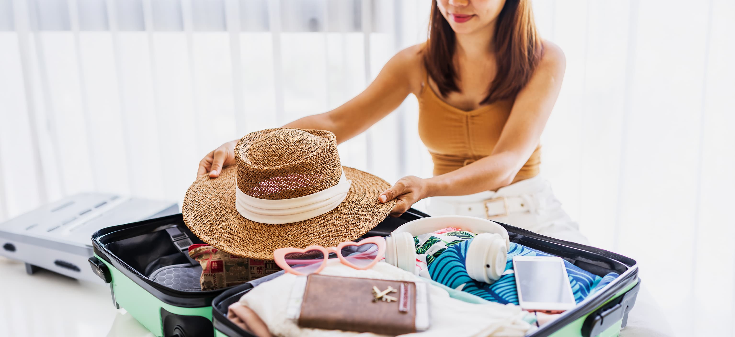 Woman packing a suitcase with a sun hat, sunglasses, and headphones