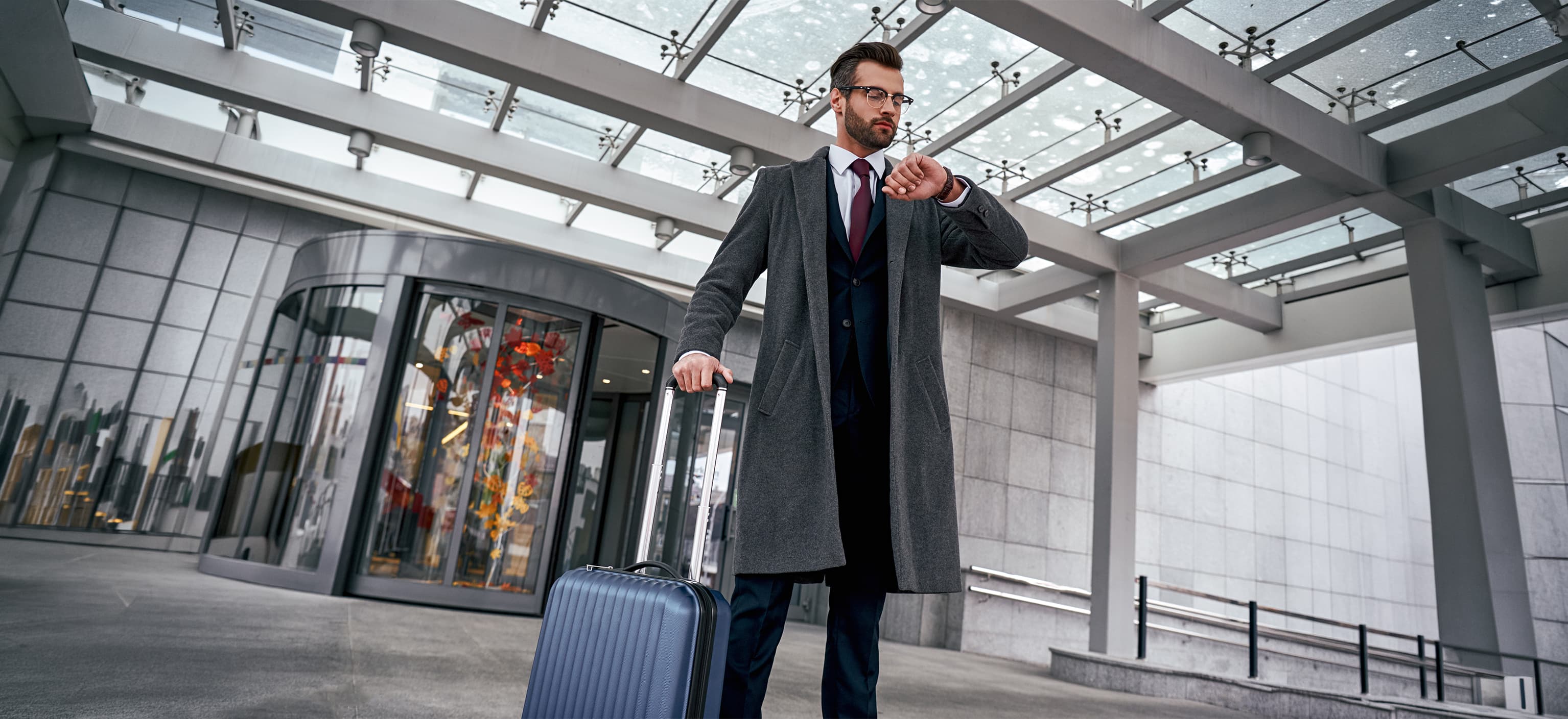 Traveler checking the time on his watch while rushing through an airport with luggage